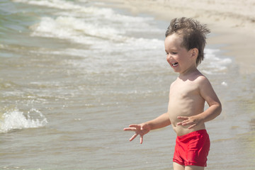 Fototapeta na wymiar Little boy enjoys the waves of the sea and laughing