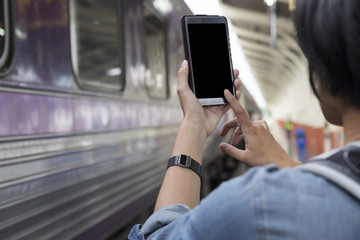 woman holding smartphone with backpack at train station