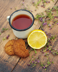 Tea in an iron mug, lemon,  oatmeal cookies, medicinal herbs on a wooden surface.
