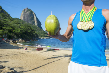 Fototapeta premium Gold medal athlete standing in front of Sugarloaf Mountain with green coconut at Red Beach in Urca, Rio de Janeiro, Brazil 