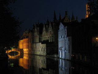 Nighttime shot of one of the canals in Bruges (Brugge) Belgium with canalside houses illuminated in different colours, which in turn are reflected in the still waters of the canal
