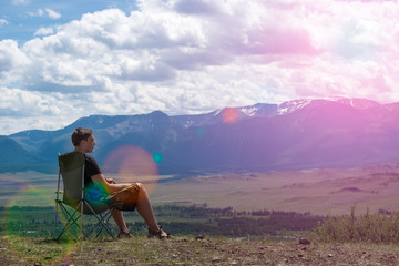 man sitting on a chair in the mountains and looks into the distance