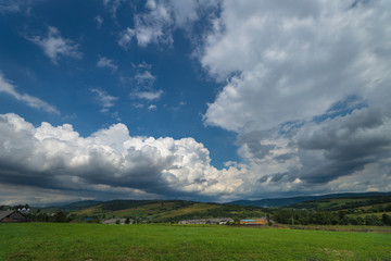 Obraz premium Natural summer landscape with green grass, blue cloudy sky and litlle houses