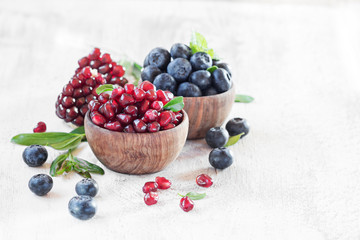 Ripe pomegranate seeds, blueberries in wooden vintage bowls with free text space. Selective focus