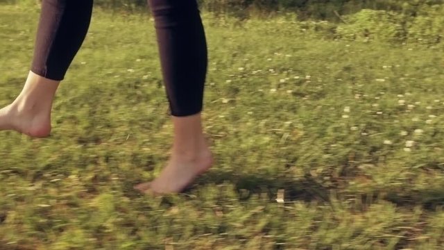 A happy young woman is jumping, playing and dancing around barefoot on grass in the summertime. Happiness, good life, relaxed lifestyle concept. Steadicam shot slow motion. Graded look.