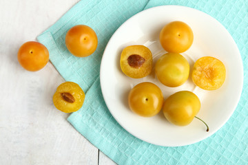 Yellow plums lying on a plate on wooden white background.