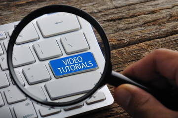 Hand Holding Magnifying Glass with "VIDEO TUTORIALS" Word On Key