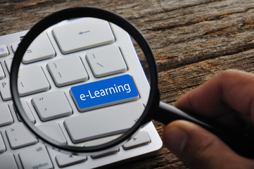 Hand Holding Magnifying Glass with "E-Learning" Word On Keyboard