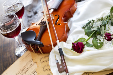 Violin, red rose, wine and music notes on satin fabric