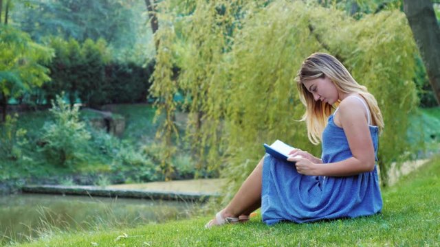 Young attractive woman reading a book in the park sitting on the grass