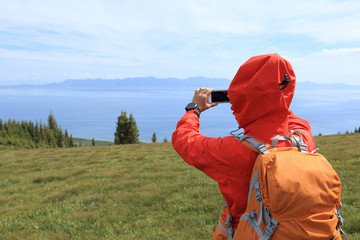 woman hiker taking photo with smart phone at mountain peak