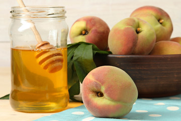 Peaches in the bowl near the jars of honey on wooden background
