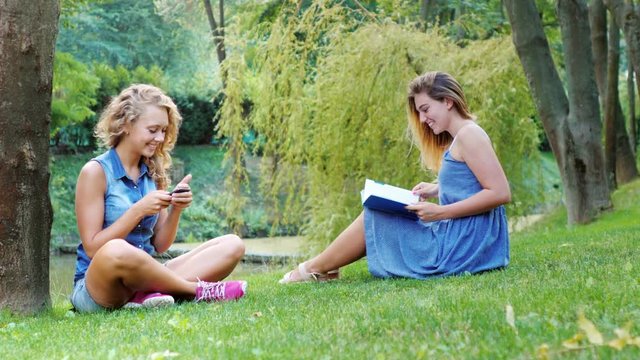 Two female friend relaxing in the park - uses the phone, read a book