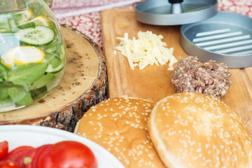 Fototapeta na wymiar Ingredients for cooking burgers. Raw ground beef meat cutlets on wooden chopping board, cherry tomatoes, cheese and lemonade on table