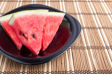 Slices of red watermelon on a black plate on a bamboo mat