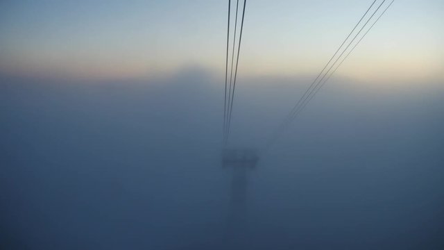 View from a cabin to a cable car tower appearing from the fog. Low visibility at mist