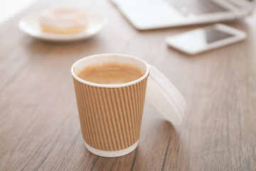Paper cup of coffee on wooden table closeup