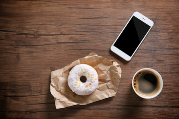 Paper cup of coffee and doughnut on wooden background