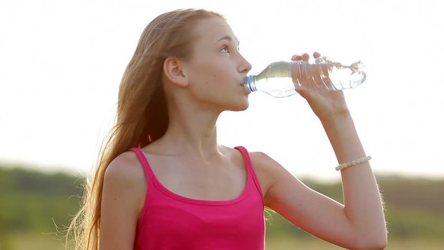 Portrait of a relaxed young girl looking away and drinking water from a plastic bottle on nature