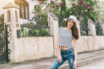 Beautiful girl in stylish jeans and white hat walking on the streets and happy.