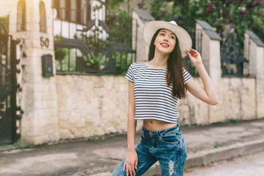 Beautiful girl in stylish jeans and white hat walking on the streets and happy.