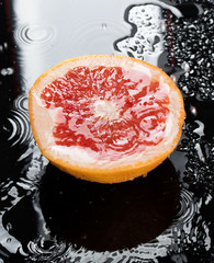 Half grapefruit citrus fruit on black background with water