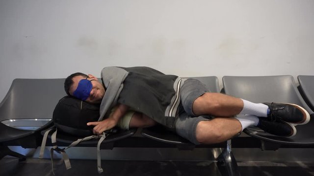 Man Traveler Backpacker Trying To Sleep At The Airport On Uncomfortable Chairs