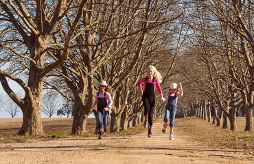 Three girls sisters running skipping down dirt road tree lined a