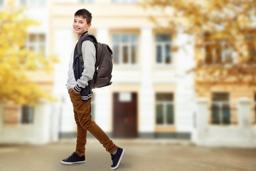 Cute little boy with grey backpack on blurred school building background