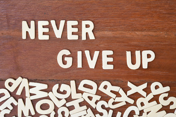 Word never give up made with block wooden letters next to a pile of other letters over the wooden board surface composition