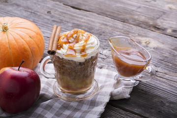 Quick breakfast snack for a few minutes in the microwave. Traditional apple pie in  mug with whipped cream quickly caramel sauce in  transparent  on  high wooden gray background. selective focus