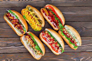 A lot of big delicious hot dogs with sauce and vegetables on wooden background. Their assorted hot dogs to gourmet. View from above.