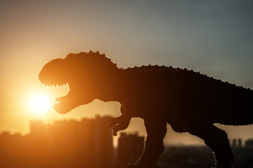 Fototapeta premium sylwetka tyranozaura i budynków w czasie zachodu słońca