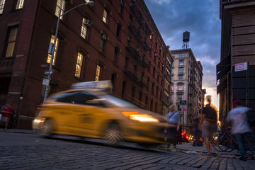 Busy street in SOHO, New York, USA with blurry people moving around and a taxi cab at sunset