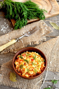 Risotto with vegetables in an earthenware bowl, fork, dill sprigs, a kitchen board on a wooden background. Rice with tomatoes, garlic, carrots and dill. Popular way of cooking rice in Italy. Top view