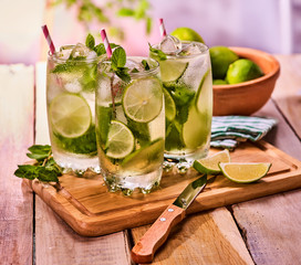 Alcohol cocktail. On wooden boards board glasses with alcohol cocktail and ice cubes. Drink number two hundred fifty one cocktail mohito with knife and mint leaf. Country still life.