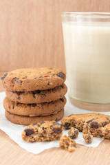 Chocolate chip cookies and a glass of milk on a wooden background.