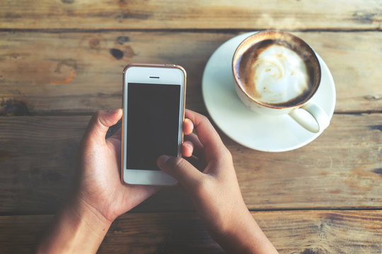 Close up of beautiful young hipster woman's hands holding mobile smart phone with hot coffee cup at cafe shop, female using cell telephone with blank copy space screen. vintage color tone