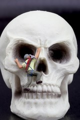 alpinisti in miniatura mentre scalano un teschio umano