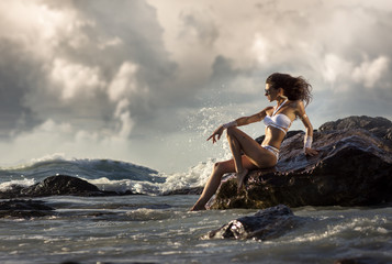 The girl in a white bathing suit sitting on a rock by the sea