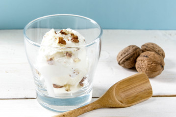 Homemade vanilla ice cream with walnuts in glass. On a white rustic wooden table.