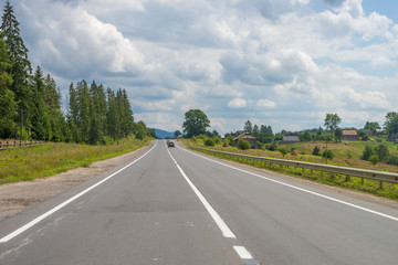 Summer day landscape with road, cloudy sky adn houses