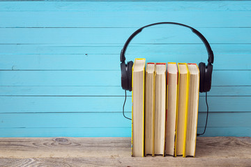 Audio book concept, yellow books and headphones over blue backgr - obrazy, fototapety, plakaty