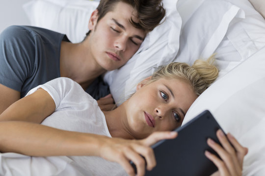 Young woman using a digital tablet with her boyfriend sleeping near her