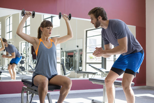 Young woman exercising with dumbbells with his trainer assisting her
