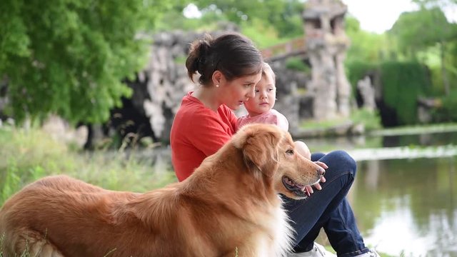Woman and baby girl playing with golden retriever dog