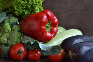 Collection of fresh ripe colorful vegetables- broccoli,red pepper,aubergine, tomatoes,squash, green salad on dark brown background.
