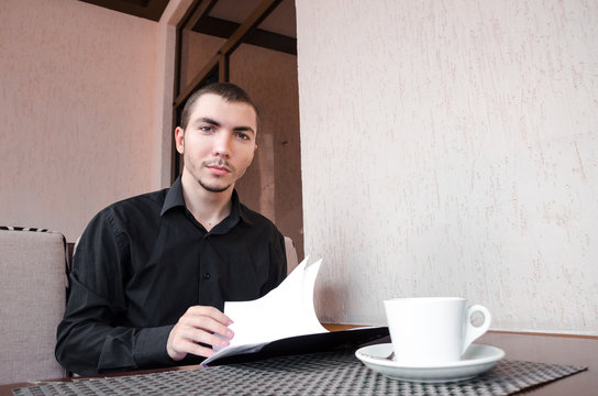 Smiling businessman drinking coffee and reading the documents.