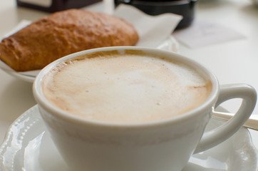 The cup of cappuccino with croissant in the background.