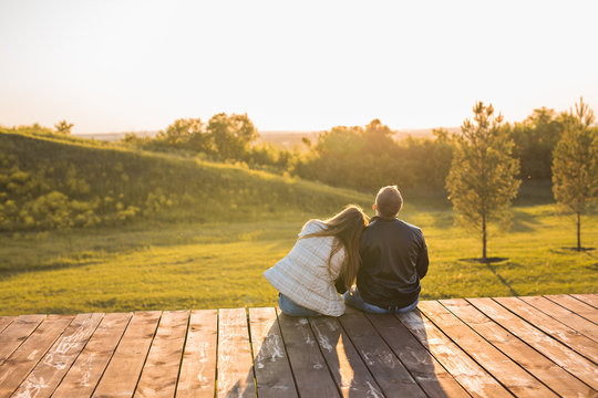 Romantic young couple enjoying autumn nature sitting in a close embrace, view from behind